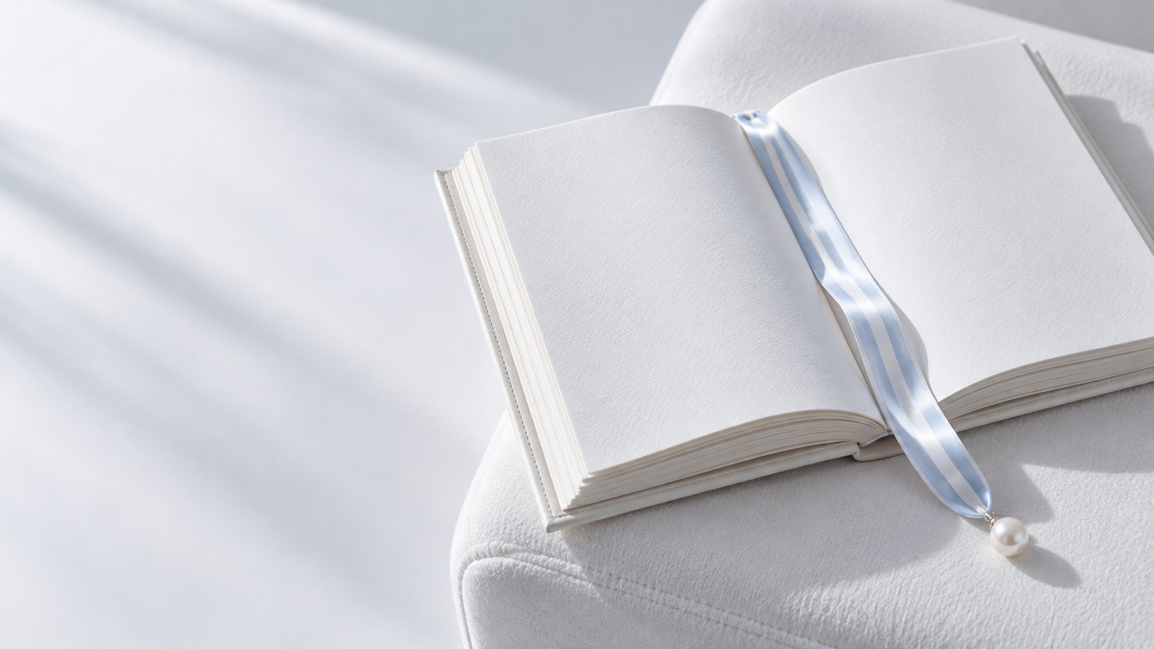 An open ivory book with blank pages and a striped ribbon bookmark finished with a pearl