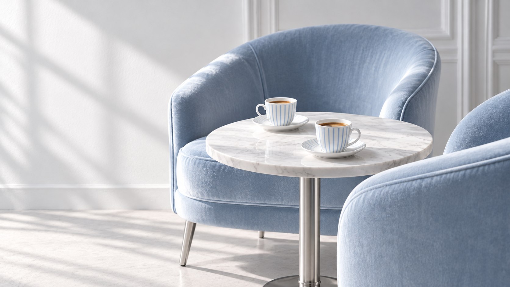 Two powder-blue velvet armchairs and striped espresso cups at a marble table
