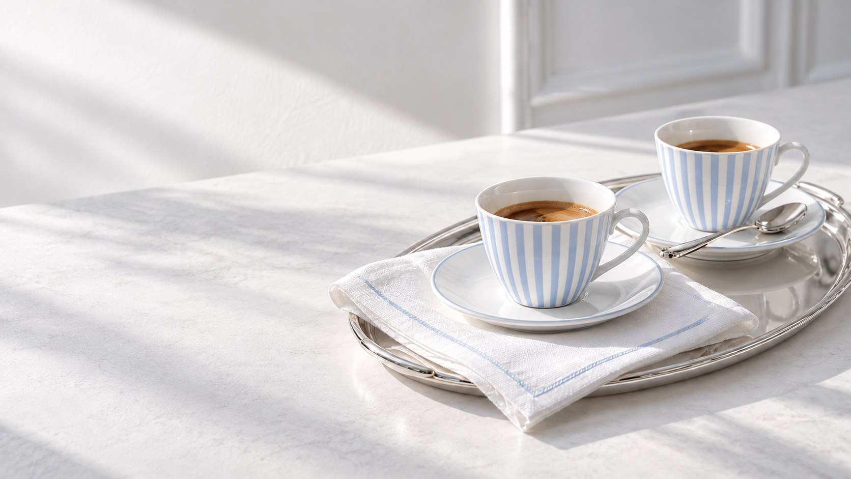 Two striped powder-blue espresso cups on a silver tray in morning light